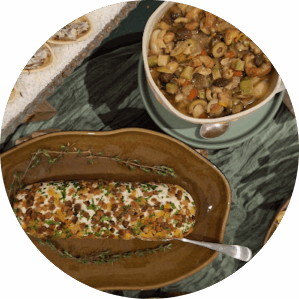 Mesa de antepastos artesanais da Alecrim com terrine decorada por ervas frescas e castanhas ao lado de um bowl com mix de azeitonas e sementes. A composição utiliza louças de cerâmica e tecidos em tons de verde, transmitindo a elegância de um evento intimista em Belo Horizonte.