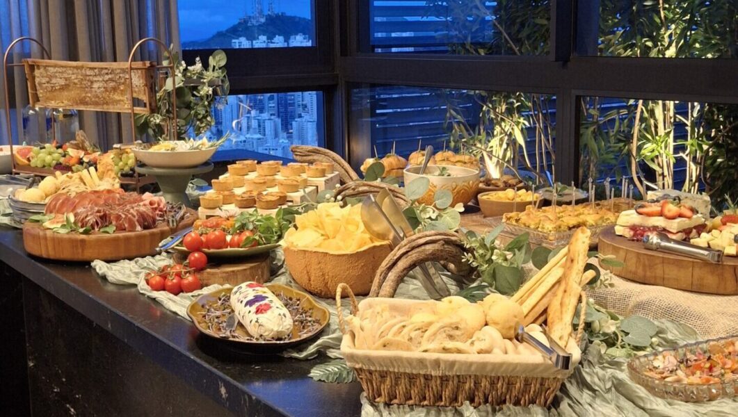 Mesa de iguarias e finger food de luxo da Alecrim Gastronomia Criativa montada para evento noturno. A Graze Table inclui pães artesanais, charcutaria, queijos finos, favo de mel, mini quiches e antepastos decorados com flores, oferecendo uma experiência de buffet sofisticada e abundante em Belo Horizonte.