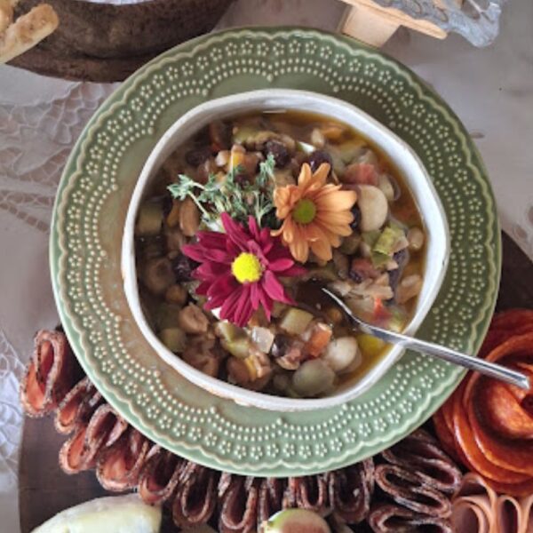 Bowl de antepasto artesanal da Alecrim composto por abobrinha, vegetais mediterrâneos, castanhas e azeitonas, decorado com flores comestíveis coloridas. A iguaria é apresentada em louças de cerâmica sofisticadas, ideal para compor mesas gastronômicas e platters em eventos intimistas.