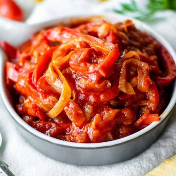 Antepasto Pepperonata da Alecrim servido em um bowl cinza, composto por tiras de pimentões vermelhos e amarelos cozidos em molho de tomate artesanal. A iguaria italiana possui textura suculenta e brilhante, ideal para acompanhar pães e compor tábuas de frios gourmet em Belo Horizonte.
