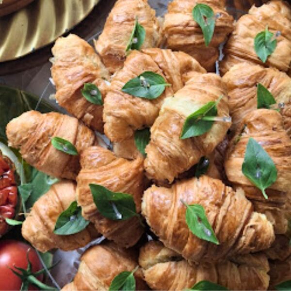 Mini croissants folhados e dourados da Alecrim, recheados ao estilo Caprese e decorados com folhas de manjericão fresco. Os mini sanduíches artesanais estão dispostos para um serviço de buffet gourmet, ideal para brunchs, eventos intimistas e coffee breaks sofisticados em Belo Horizonte.