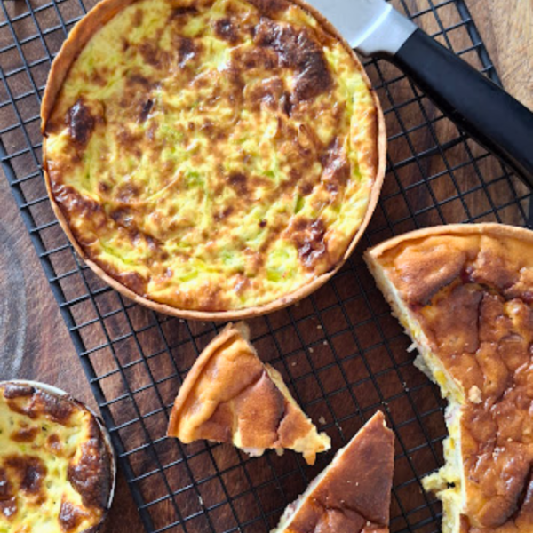 Quiche artesanal de bacalhau da Alecrim com recheio alto e dourado, apresentada sobre uma grade metálica e mesa de madeira. Uma fatia cortada revela a textura cremosa do prato, ideal para brunchs, eventos intimistas e celebrações em Belo Horizonte que valorizam a gastronomia afetiva.