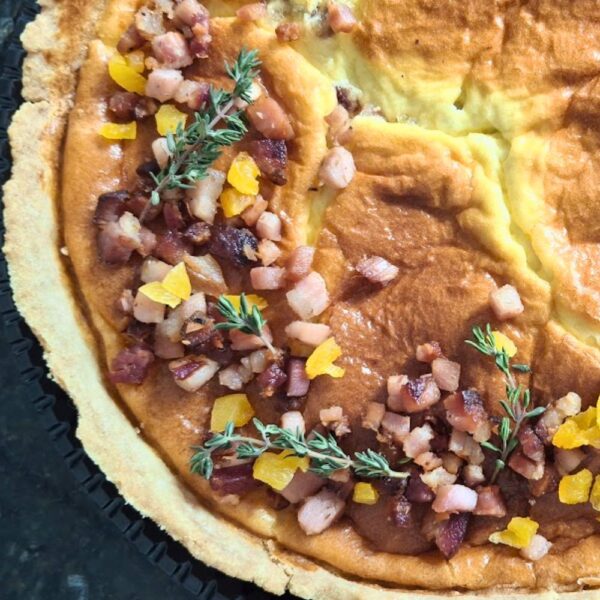 Quiche artesanal da Alecrim com recheio alto e dourado, coberta com cubos de bacon crocante, pedaços de damasco suculento e ramos de tomilho fresco. A torta gourmet exemplifica a gastronomia criativa da marca para eventos intimistas e recepções sofisticadas em Belo Horizonte.