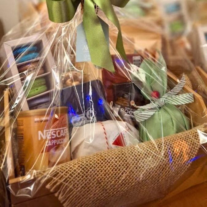 Cesta de café da manhã artesanal Alecrim em embalagem sofisticada com laço de cetim verde e buquê de flores secas. No interior, produtos gourmet como macarons coloridos, cappuccino, pães artesanais envoltos em tecido e antepastos, transmitindo uma experiência de presente afetuoso e sofisticado em Belo Horizonte.