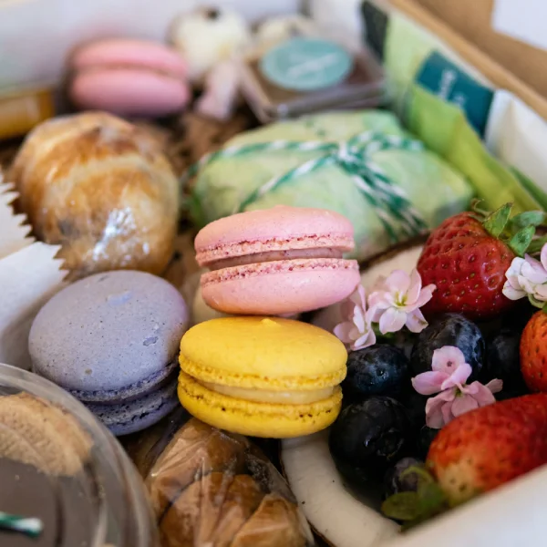 Detalhe de itens gourmet da cesta de café da manhã premium Alecrim. A foto destaca macarons artesanais, frutas vermelhas frescas e pães delicados organizados com olhar estético. Este nível de curadoria gastronômica em BH é pensado para anfitriões e presenteadores que valorizam o sabor autoral e a beleza em cada detalhe.