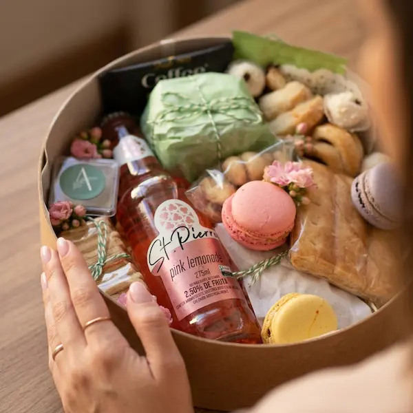 caixa redonda de presente fino contendo pink lemonade, croissant, broa de milho, macarons, biscoitos amanteigados, cafe, decoração