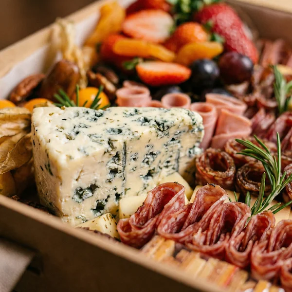 Experiência gourmet 'Quer Vin? Vem!' da Alecrim Gastronomia Criativa. Caixa de madeira artesanal com vinho importado, duas taças de vidro e tábua de charcutaria completa com queijos, salames, pães, antepastos e frutas frescas como morangos e physalis, decorada com alecrim.