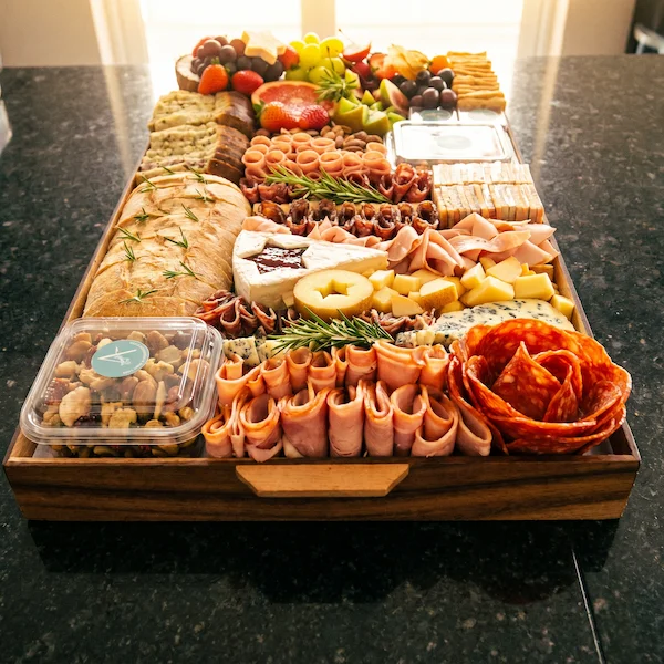 Tábua de frios de luxo, composta por charcutaria selecionada, queijos finos, torradas, pesto, castanha, morango e uvas.