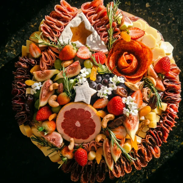 Tábua de frios de luxo, composta por charcutaria selecionada, queijos finos, torradas, pesto, castanha, morango e uvas.