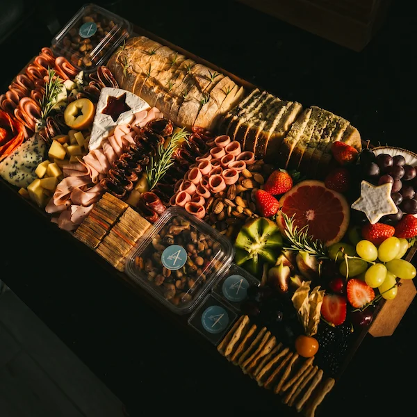 Tábua de frios de luxo, composta por charcutaria selecionada, queijos finos, torradas, pesto, castanha, morango e uvas.