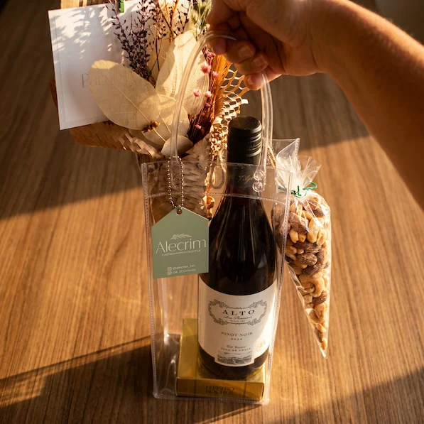 Presente elegante com vinho tinto, mix de nuts e chocolates em sacola transparente de PVC decorada artesanalmente pela Alecrim.