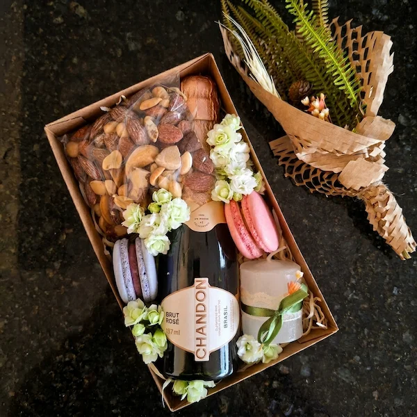 Caixa presente delicada com espumante baby, macarons, mix de nuts e vela artesanal em embalagem kraft decorada com flores.