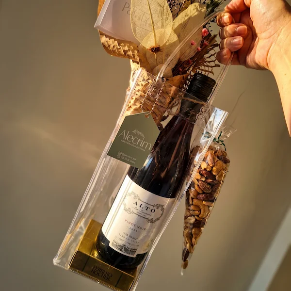 Detalhe de garrafa de vinho fino importado acompanhada por um delicado mini arranjo de flores desidratadas e tag artesanal personalizada.