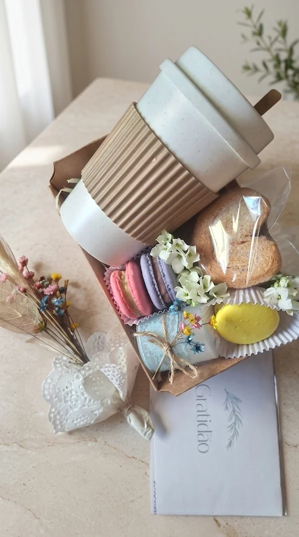 presente delicado com café e doces da Alecrim Gastronomia Criativa em BH, contendo copo térmico branco com luva marrom, macarons coloridos, biscoitos artesanais e tag de agradecimento 'Gratidão', sobre bancada de granito com luz solar natural.