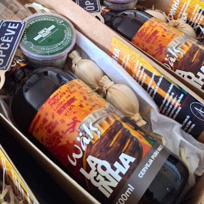 Sequência de caixas de presente kraft da Alecrim alinhadas, contendo cerveja artesanal Wäls Lagoinha, geleia de cachaça e petiscos artesanais. As caixas possuem tags com a expressão mineira "Ôpcêvê", unindo a cultura de Belo Horizonte a um design de presente sofisticado e criativo para happy hour.