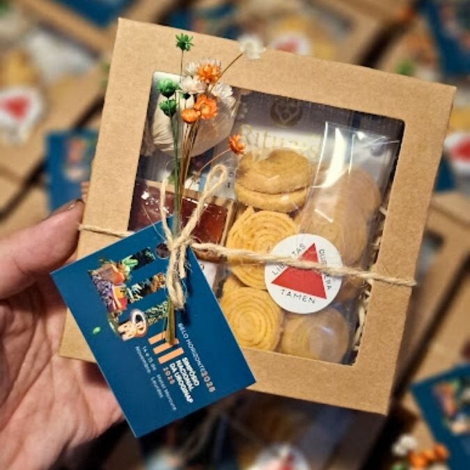 kit presenteável Mineirinho da Alecrim em caixa kraft com visor, contendo biscoitos artesanais e doce típico. A embalagem é finalizada com cordão de juta, flores secas e tag personalizada para evento corporativo, destacando a gastronomia afetiva e a identidade local de Belo Horizonte.
